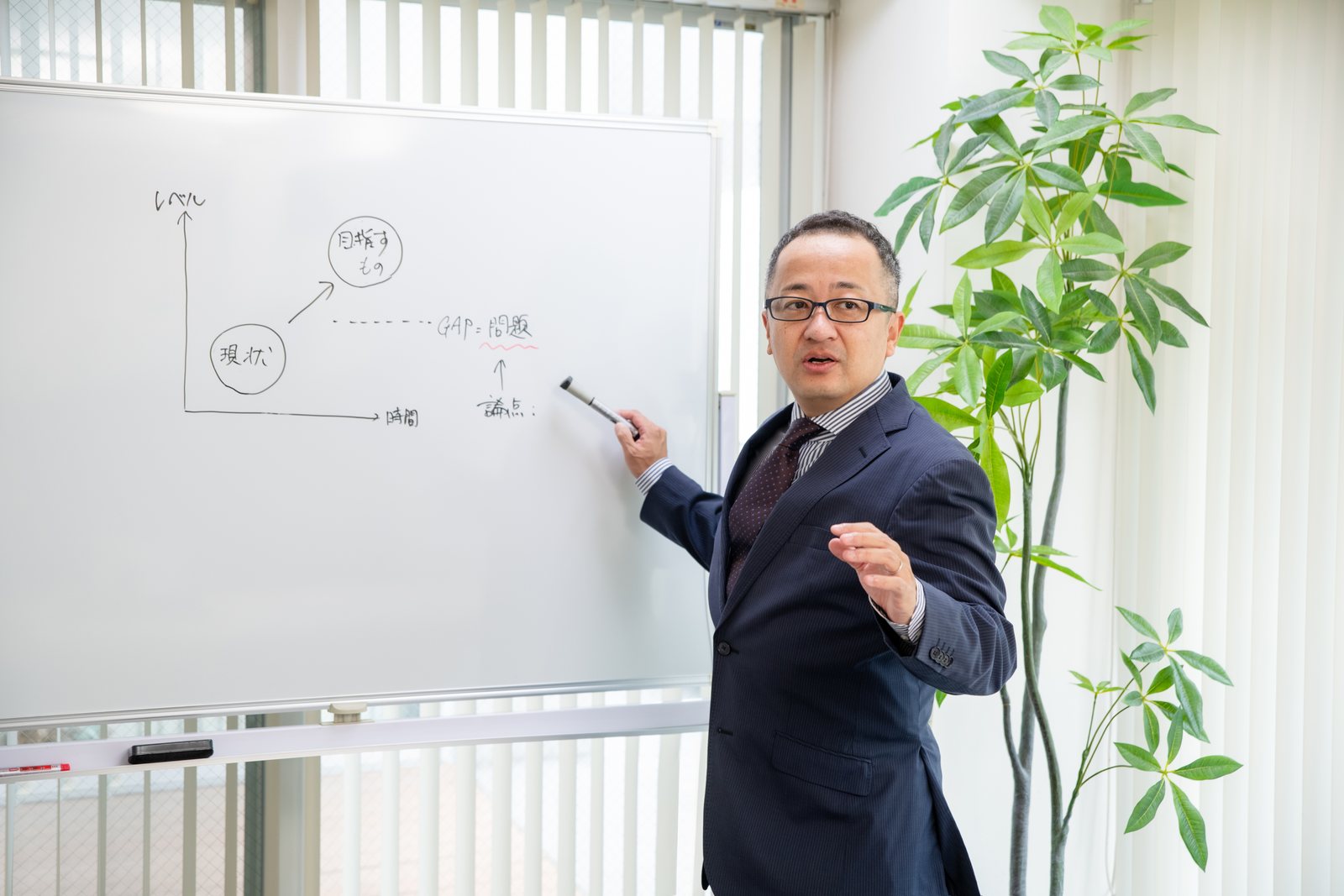 ホワイトボードに業務の流れ図を描いて説明する唐澤智哉